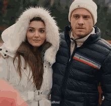 a man and woman standing next to each other in the park wearing winter ...
