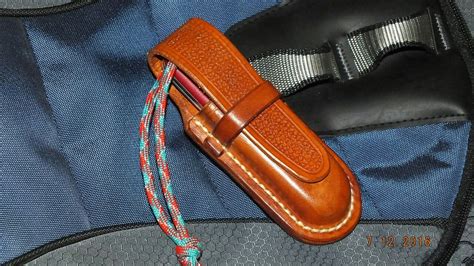 a brown leather knife case sitting on top of a blue and gray backpack with a rope