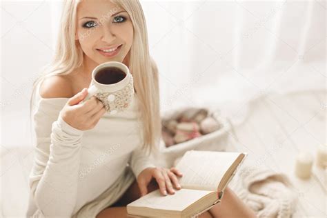 The girl is drinking coffee and reading a book at home — Stock Photo © golyak #57906381