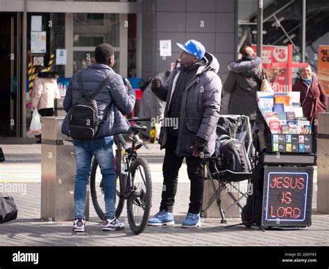 Christian street preacher, with Jesus is Lord neon sign, preaching to passing shoppers and ...