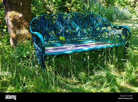 A pretty rustic wrought iron bench or seat in a shady corner of an English country garden in ...