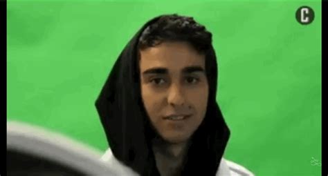 a man wearing a black hoodie and looking at the camera with a green screen behind him