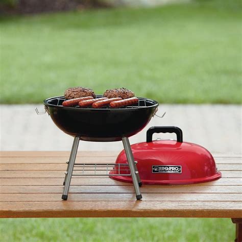 a grill with hot dogs on it sitting on a picnic table next to a red kettle