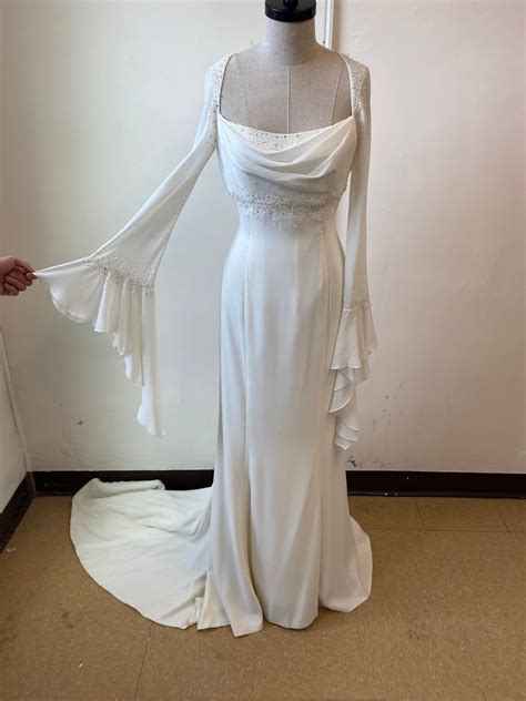 a white wedding dress on display in front of a wall with a mannequin