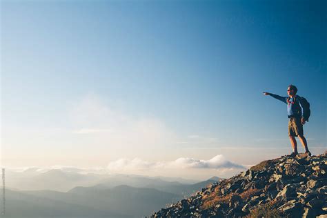 "Man Standing On Mountain Summit, Pointing Towards Mountains And Sky ...