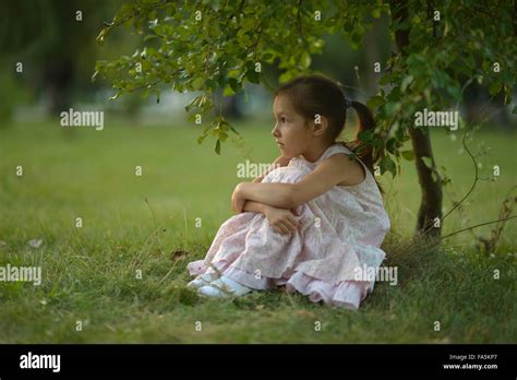 Little girl sitting under tree Stock Photo - Alamy