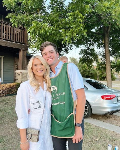 a man and woman standing next to each other in front of a house with cars