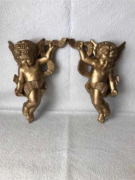 two gold angel figurines sitting on top of a white sheet