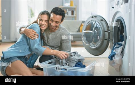 Beautiful Young Couple Sit Next to a Washing Machine at Home. They Laugh and Embrace While ...