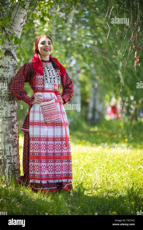 Young woman in traditional russian clothes standing in the forest and holds hands on a waist ...