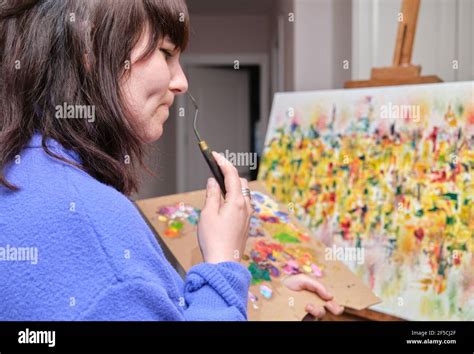 Young woman thinking and painting on canvas with oil paints at home. Artist drawing on easel ...