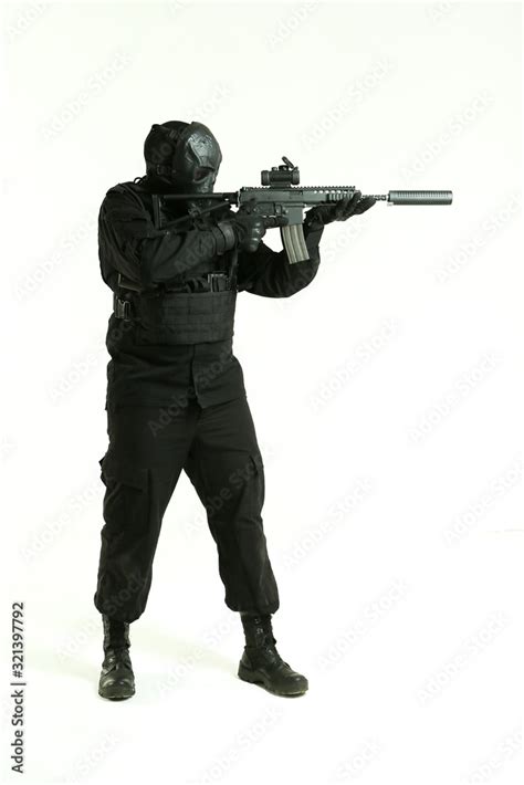 a man in a black military uniform and mask of cyborg aiming an machine gun and standing full ...