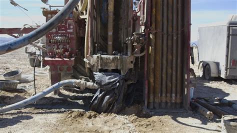 Drill rig extracting liquid from beneath salt flats with workers in background | ClipStock