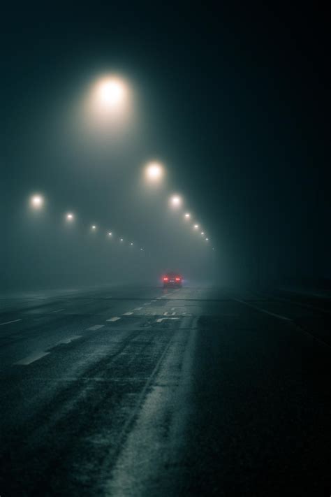 a foggy night with street lights and cars driving down the road in the snow