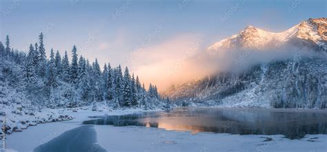 Sunrise in winter mountains. Mountain reflected in ice lake in morning sunlight. Amazing ...