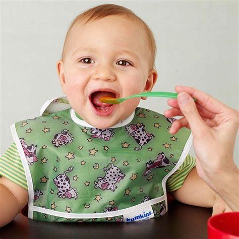 a baby sitting at a table with a spoon in it's mouth while being fed