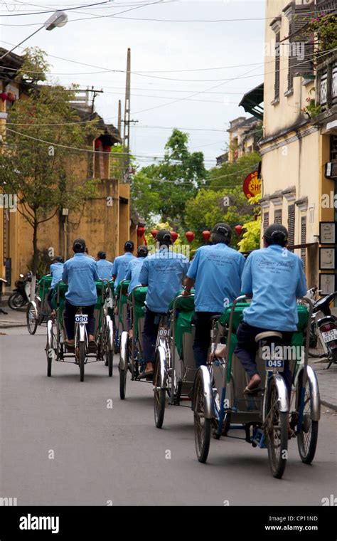 A group of Tuk Tuk drivers couriering people through the high street in Hoi An old town, Vietnam ...