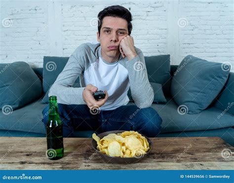 Bored Young Man Sitting on the Couch Watching TV Switching Channels Looking for Live Sports ...