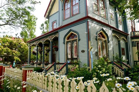 a blue house with red trim and white daisies in the foreground, on a sunny day