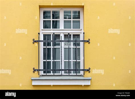 Window with a white rectangular frame and binding, located on the yellow wall of the house and ...