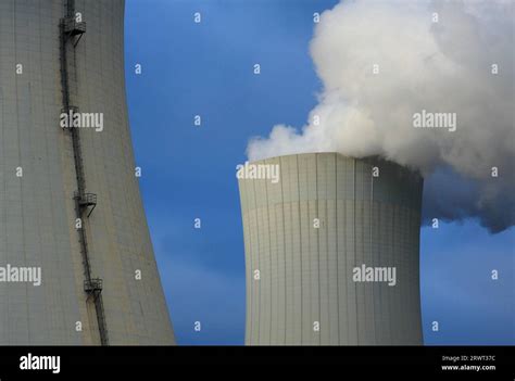 Two cooling towers, one of which emits water vapour, background blue ...