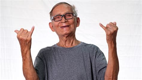 Funny grandfather in gray t-shirt and glasses showing hand gesture on white background in studio ...