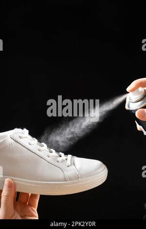Woman applying water repellent spray on black shoes near color wall Stock Photo - Alamy