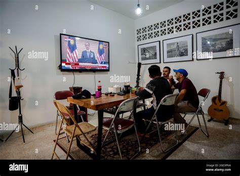 People watch Prime Minister Muhyiddin Yassin's speech on a TV screen in ...