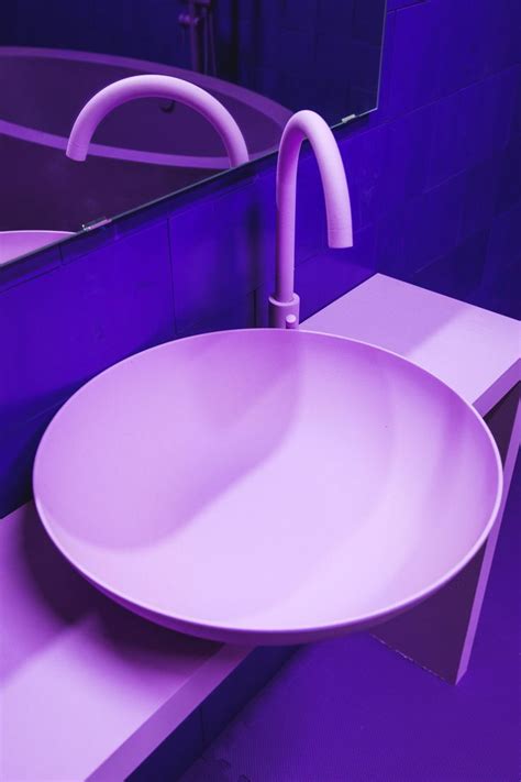 a white sink sitting on top of a counter next to a purple wall mounted mirror