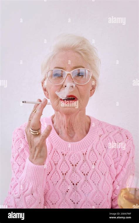 Old fashioned senior stylish woman smoking cigarette with glass of white wine. Bad habit ...