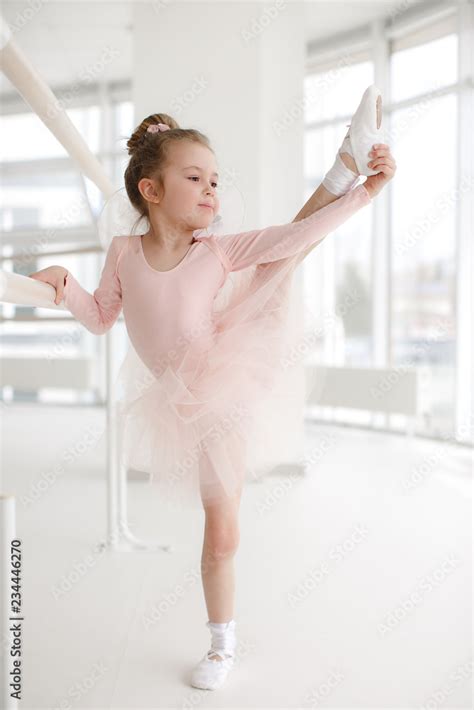 Little ballerina girl in a pink tutu. Adorable child dancing classical ballet in a white studio ...