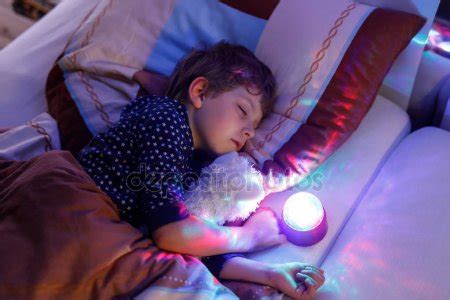 Little preschool kid boy sleeping in bed with colorful lamp. School child dreaming and holding ...