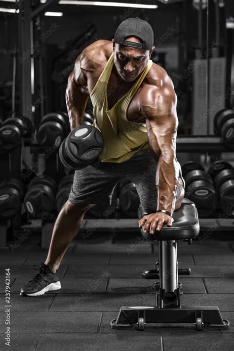 Muscular man working out in gym doing exercises for back. Single Arm Dumbbell Row Stock Photo ...