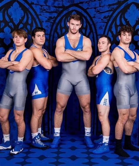 four men in blue and grey wrestling uniforms posing for a photo with their arms crossed