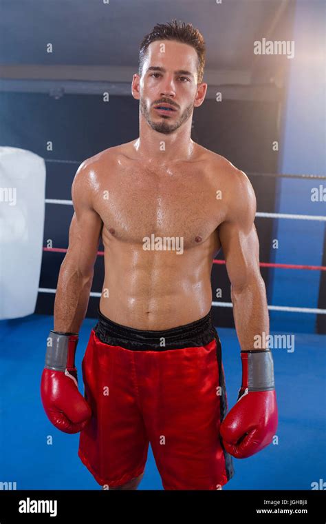 Portrait of confident male boxer wearing red gloves standing in boxing ...