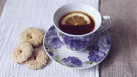 a cup of tea and two donuts on a tablecloth with a white cloth