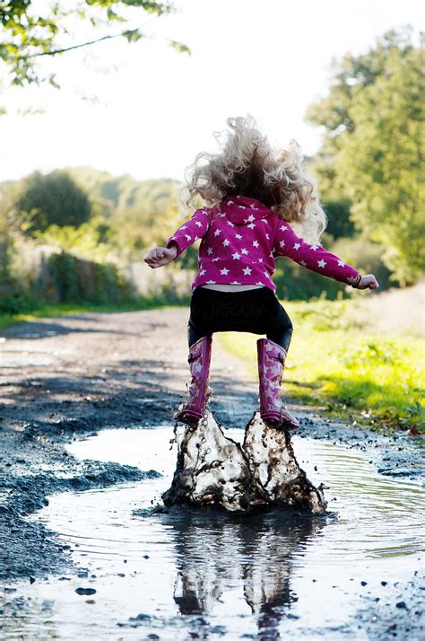 "Girl Jumping In A Muddy Puddle" by Stocksy Contributor "CHRISTINA K" - Stocksy