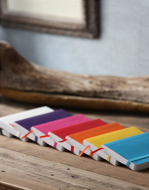 a row of colorful notebooks sitting on top of a wooden table next to a ...