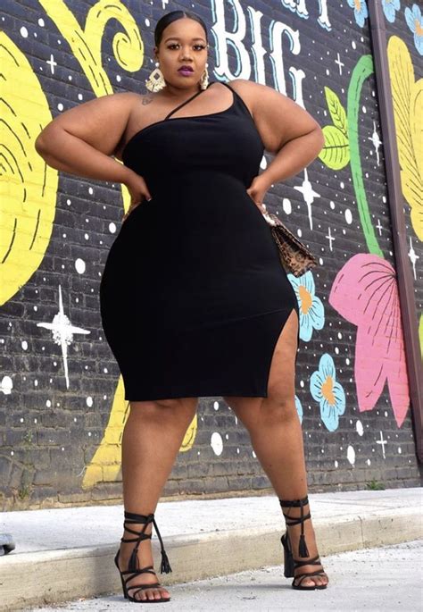 a woman standing in front of a wall wearing a black dress and high heeled sandals