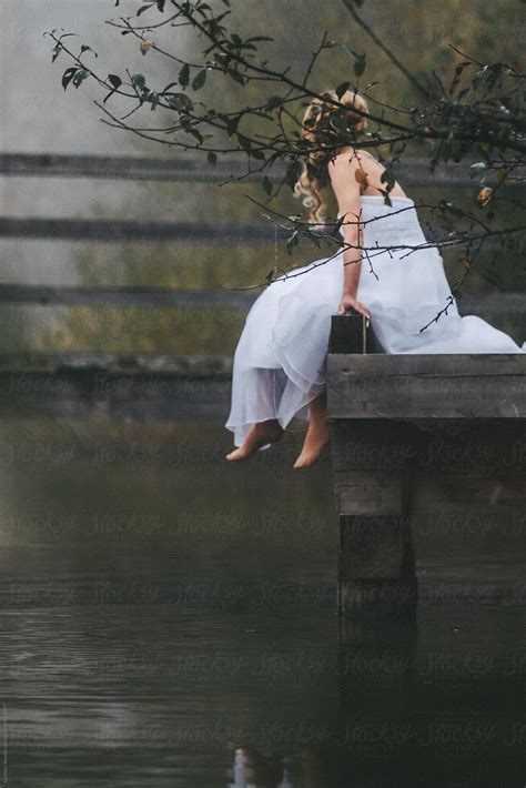 "Barefoot Bride In Beautiful White Wedding Dress Sitting On A Jetty In Foggy Landscape" by ...