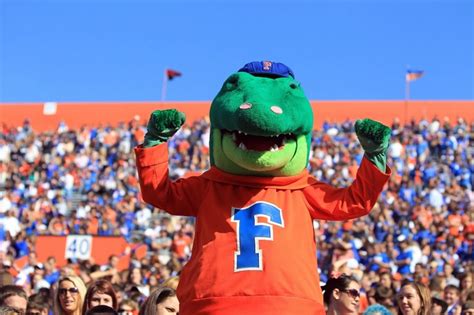 a man in an orange shirt and green alligator costume at a football game with the number 1 on his ...