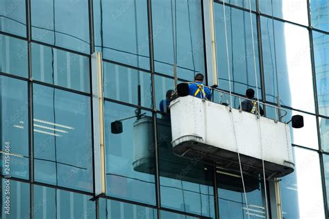 Workers crane cradle clean windows glass of high building under sun day light blur sky, Hoist ...