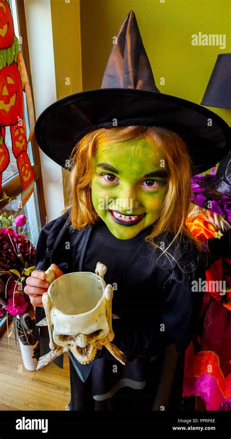 Girl child with a green face, face paint, dressed in a kid Halloween witch costume, wearing a ...