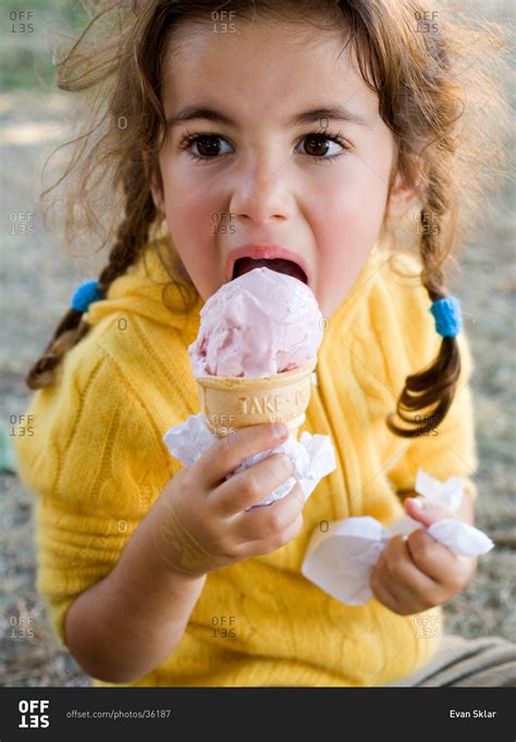 Young girl eating strawberry ice cream from a cone stock photo - OFFSET