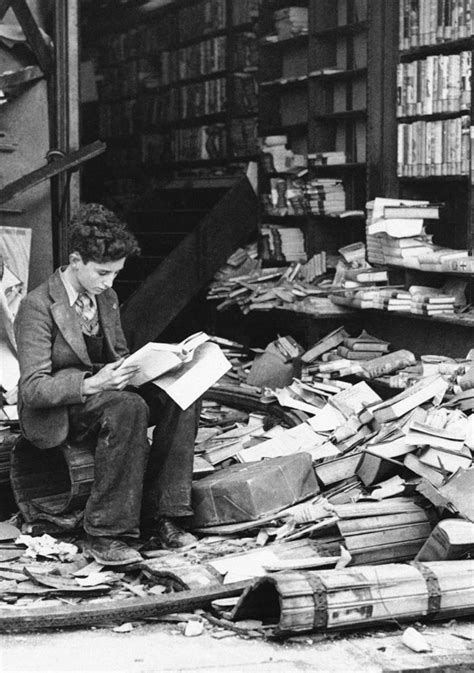 A young British boy sits reading outside the ruins of a bookshop that suffered Luftwaffe bomb ...