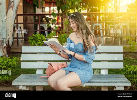 A cute girl sitting on a bench reading a book Stock Photo - Alamy