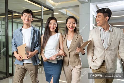 Happy young professional asian business people holding clipboards and smiling at camera while ...