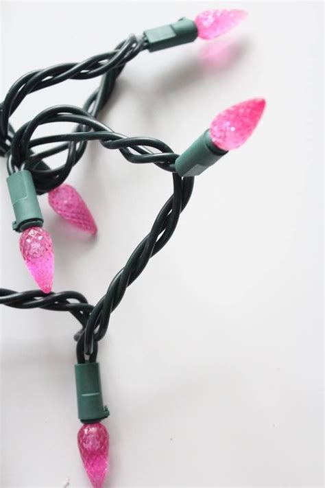 pink and green christmas lights are on a white surface with black wire wrapped around them