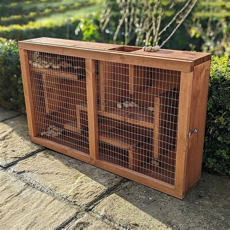 a wooden cabinet with metal mesh doors and drawers on the bottom, in front of some bushes