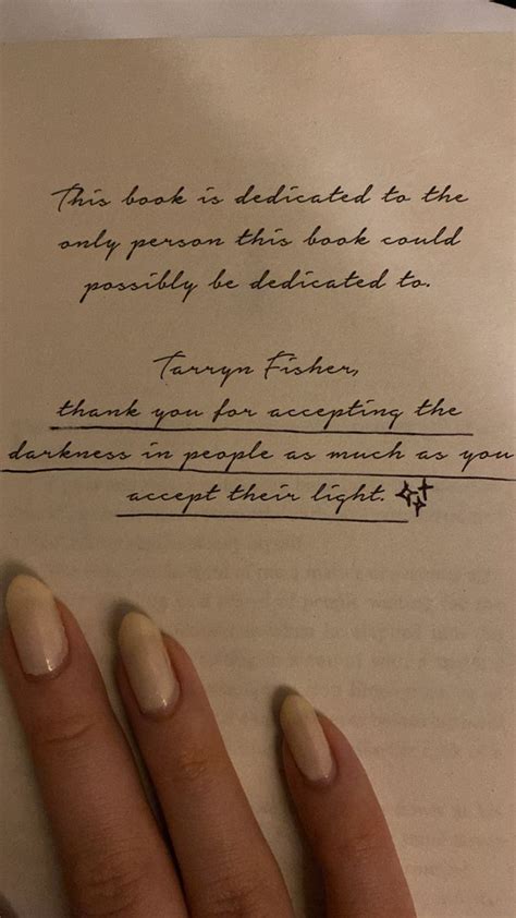 a woman's hand holding an open book with writing on the page next to her